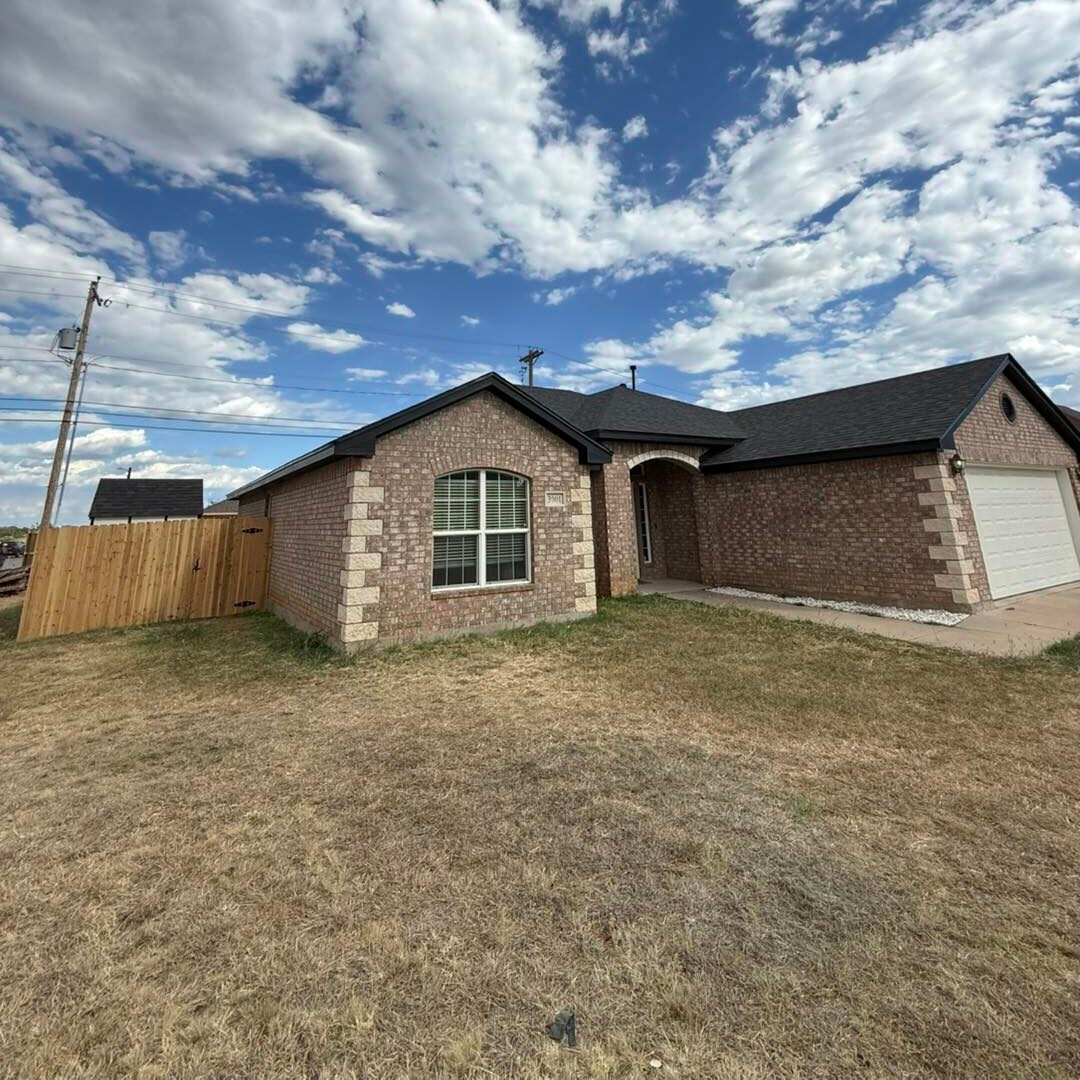 Residential roof replacement on a brick home with dark shingles under a West Texas sky in Abilene, TX.