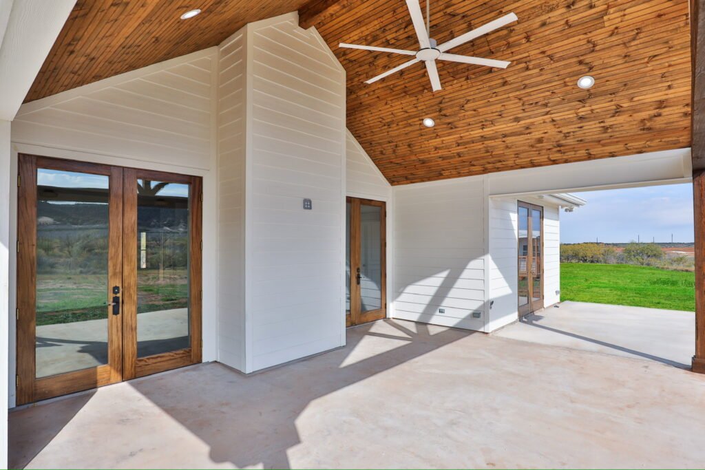 “Covered outdoor living space with wood-plank ceiling, modern ceiling fan, and large glass doors for a seamless transition to the yard.”